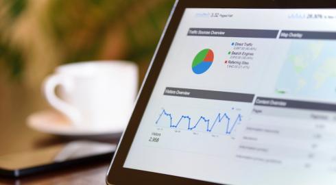 Close up of laptop monitor with a mobile device and coffee cup behind