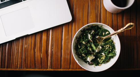 Bowl of greens next to a laptop and a coffee cup