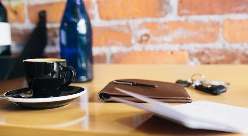 Coffee cup, note pads, keys and a glass bottle on a wooden surface