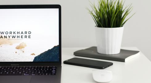 Open laptop on a table with a mouse, mobile device and small potted plant